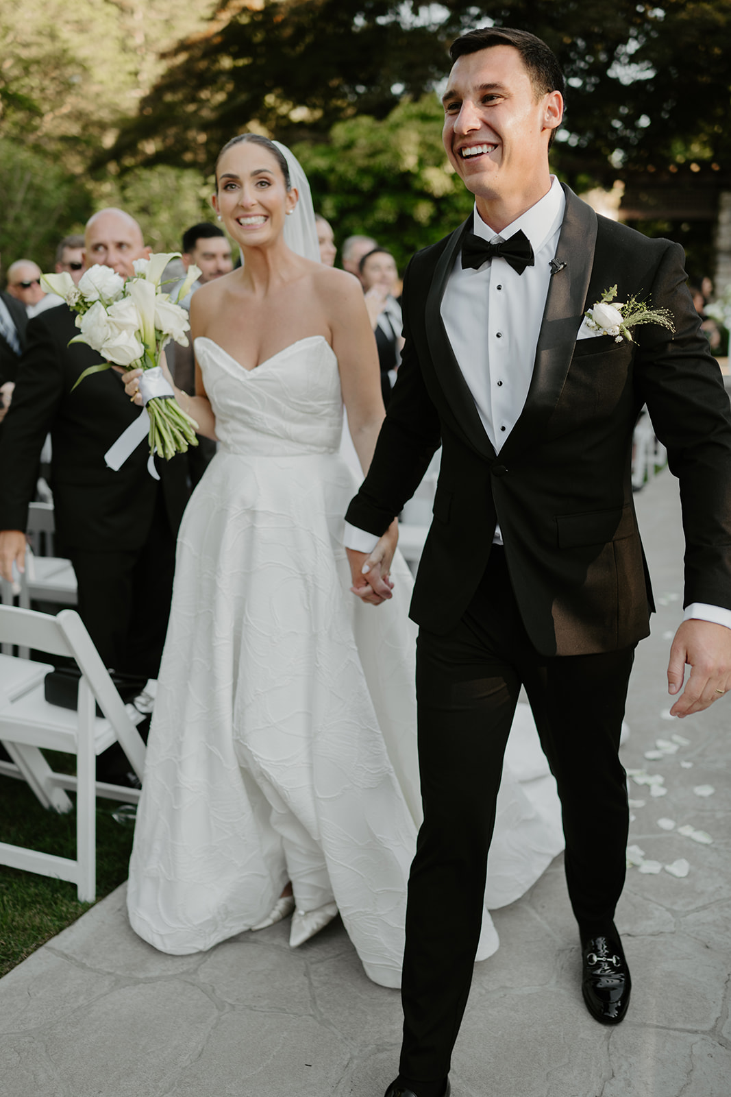 Newlyweds walking down the aisle hand-in-hand, laughing and smiling in pure joy after their ceremony.